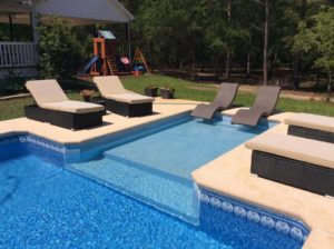 An in-ground pool with relaxing pool-side furniture.